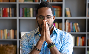 Photo of man sitting at desk and either thinking or praying.
